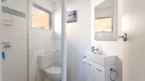 Un baño con inodoro, lavabo y ducha. Hay una ventana sobre el inodoro y un espejo sobre el lavabo.
