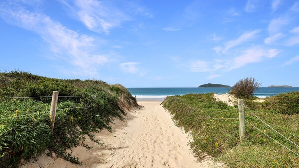 A sandy beach path leading to the ocean with a clear sky and distant islands. - Surfs Up - moments from the sands of Bennett’s Beach (Hawks Nest)