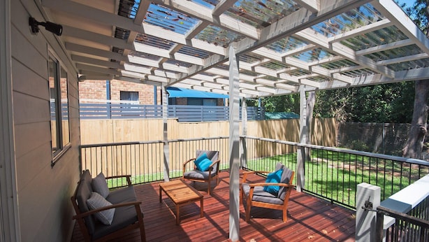Eine überdachte Terrasse mit Holzmöbeln, einer Pergola und Blick auf einen Garten.
