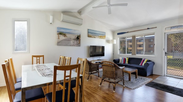 A modern living room with a dining area, featuring a TV, comfortable seating, and artwork on the walls.