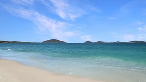 Una playa con agua turquesa cristalina, una orilla de arena y islas a lo lejos.