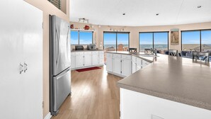 Una cocina moderna con armarios blancos, electrodomésticos de acero inoxidable y ventanas amplias con vista al océano.