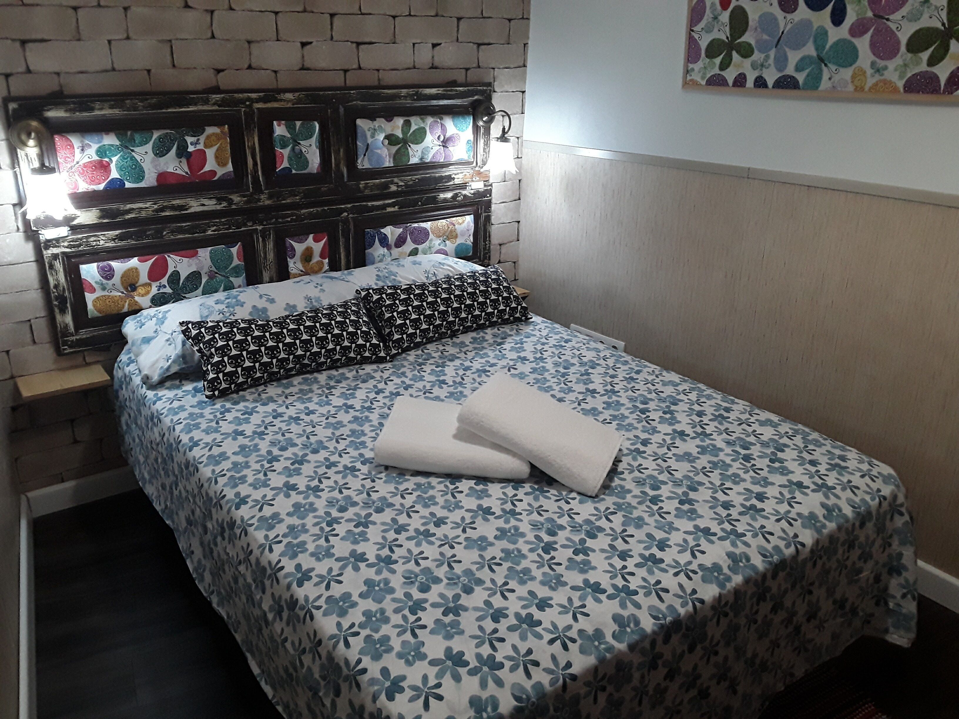 A neatly made bed with a floral bedspread, a patterned pillow, and two folded towels. - IN THE HEART OF GRANADA - WIFI (Granada)