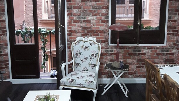 A room with a brick wall, a white chair with floral upholstery, a small table with a plant, and a window with a view of the outside. - IN THE HEART OF GRANADA - WIFI (Granada)