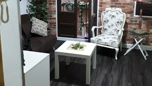 A room with a brick wall, a white chair with floral upholstery, a small table with a plant, a brown sofa with a patterned pillow, and a door leading outside. - IN THE HEART OF GRANADA - WIFI (Granada)