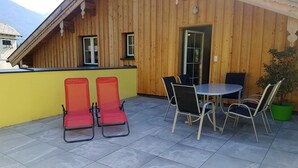 Un bâtiment en bois doté d’un balcon, deux chaises rouges, une table avec quatre chaises et une plante en pot.