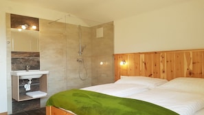 Une chambre à coucher avec une tête de lit en bois, une couverture verte, un lit blanc, une armoire en bois avec un lavabo et une douche.