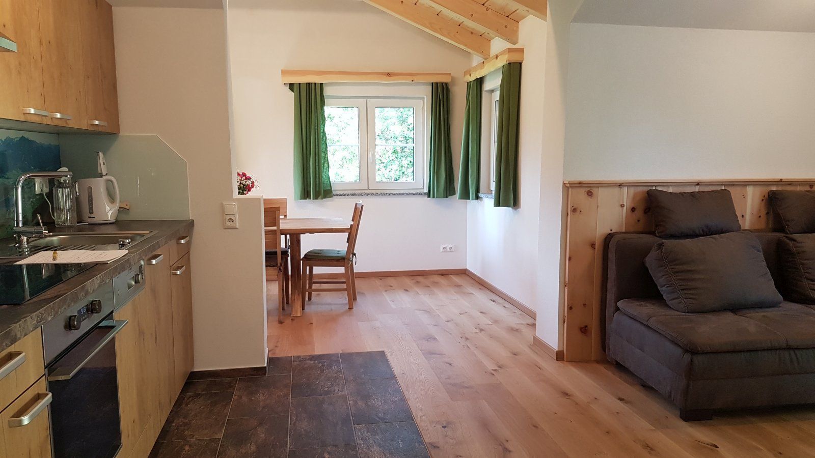 A kitchen with a stove, sink, and cabinets, a dining area with a table and chairs, and a sofa in a living area.