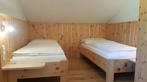 Une petite pièce en bois avec deux lits simples, chacun doté d’une tête de lit en bois et d’une table de chevet.