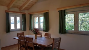 Un coin repas avec une table et des chaises en bois, un vase rempli de fleurs et de grandes fenêtres ornées de rideaux verts.