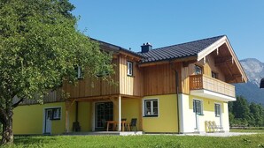 Une maison en bois à deux étages, dotée d’un balcon, d’un porche couvert et surplombant un paysage montagneux.