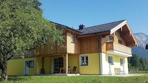 Une maison en bois à deux étages, dotée d’un balcon, d’un porche couvert et surplombant un paysage montagneux.