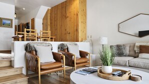 Una sala de estar moderna con una pared de madera, sofás de cuero, una mesa de centro con revistas y una planta en maceta.