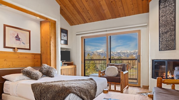 Un dormitorio con una cama grande, techo de madera, chimenea y balcón con vistas a la montaña.