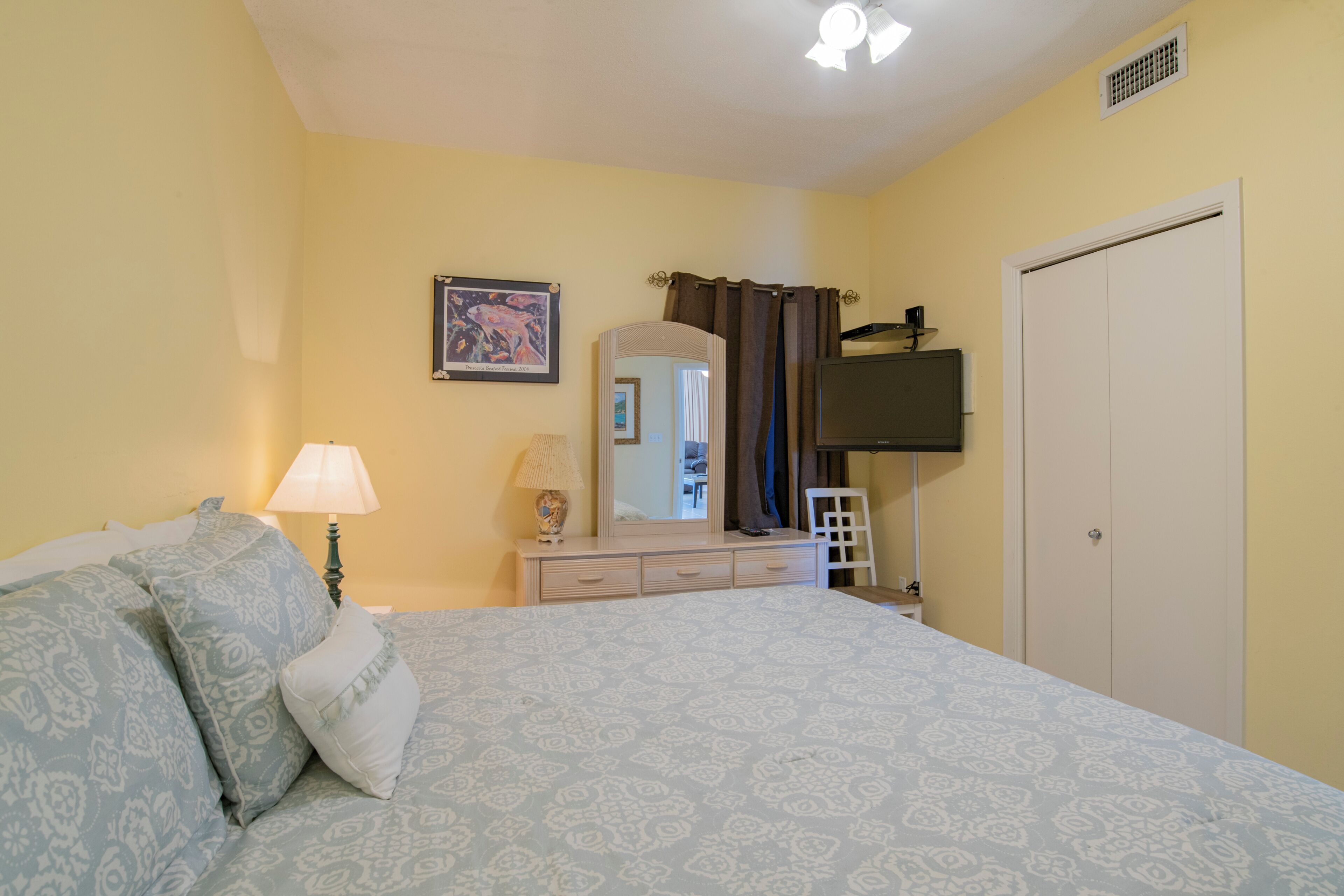Un dormitorio con cama, cómoda, espejo y televisor en la pared.