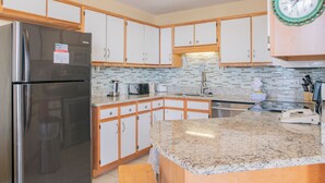 A modern kitchen with stainless steel appliances, white cabinets, and a granite countertop. - Beachfront One Bedroom Sleeps Six (Orange Beach)