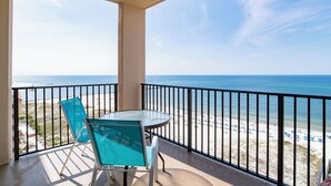 A balcony with a glass table and chairs overlooking a beach with a clear sky. - Beachfront One Bedroom Sleeps Six (Orange Beach)