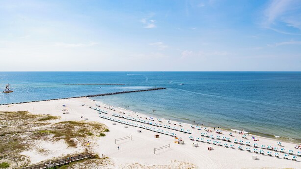 A beach with rows of beach umbrellas and sun loungers, a pier extending into the water, and a sandy walkway. - Beachfront One Bedroom Sleeps Six (Orange Beach)