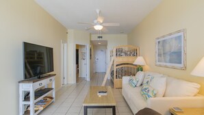 A living room with a television, a wooden coffee table, a white sofa, a brown leather couch, a wooden crib, and a ceiling fan. - Beachfront One Bedroom Sleeps Six (Orange Beach)