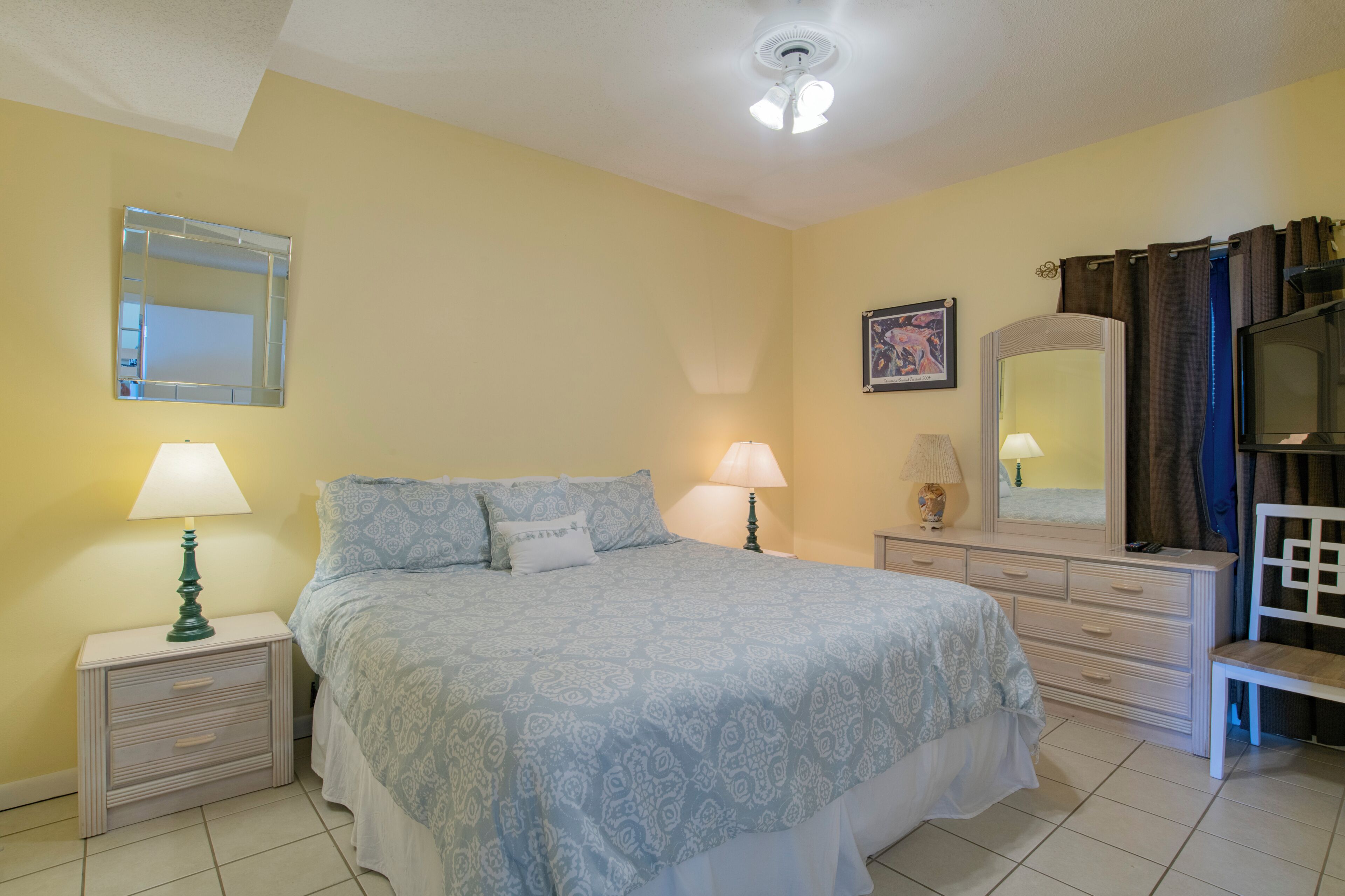 A bedroom with a bed, two bedside tables with lamps, a dresser, a mirror, and a chair.