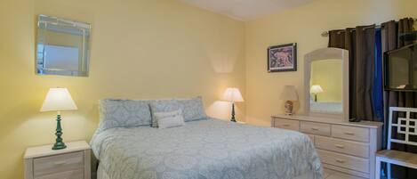 A bedroom with a bed, two bedside tables with lamps, a dresser, a mirror, and a chair.