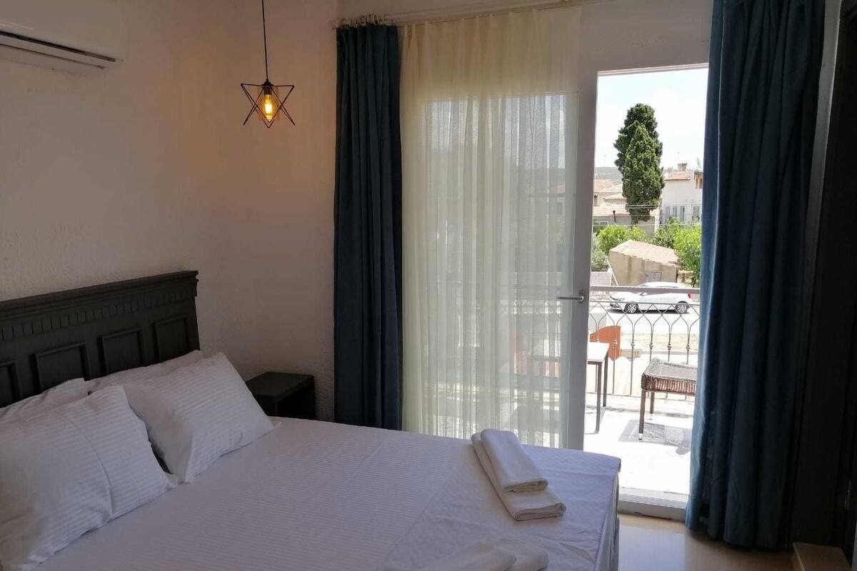 Habitación de hotel con cama, mesita de noche, lámpara colgante y vistas al balcón exterior.