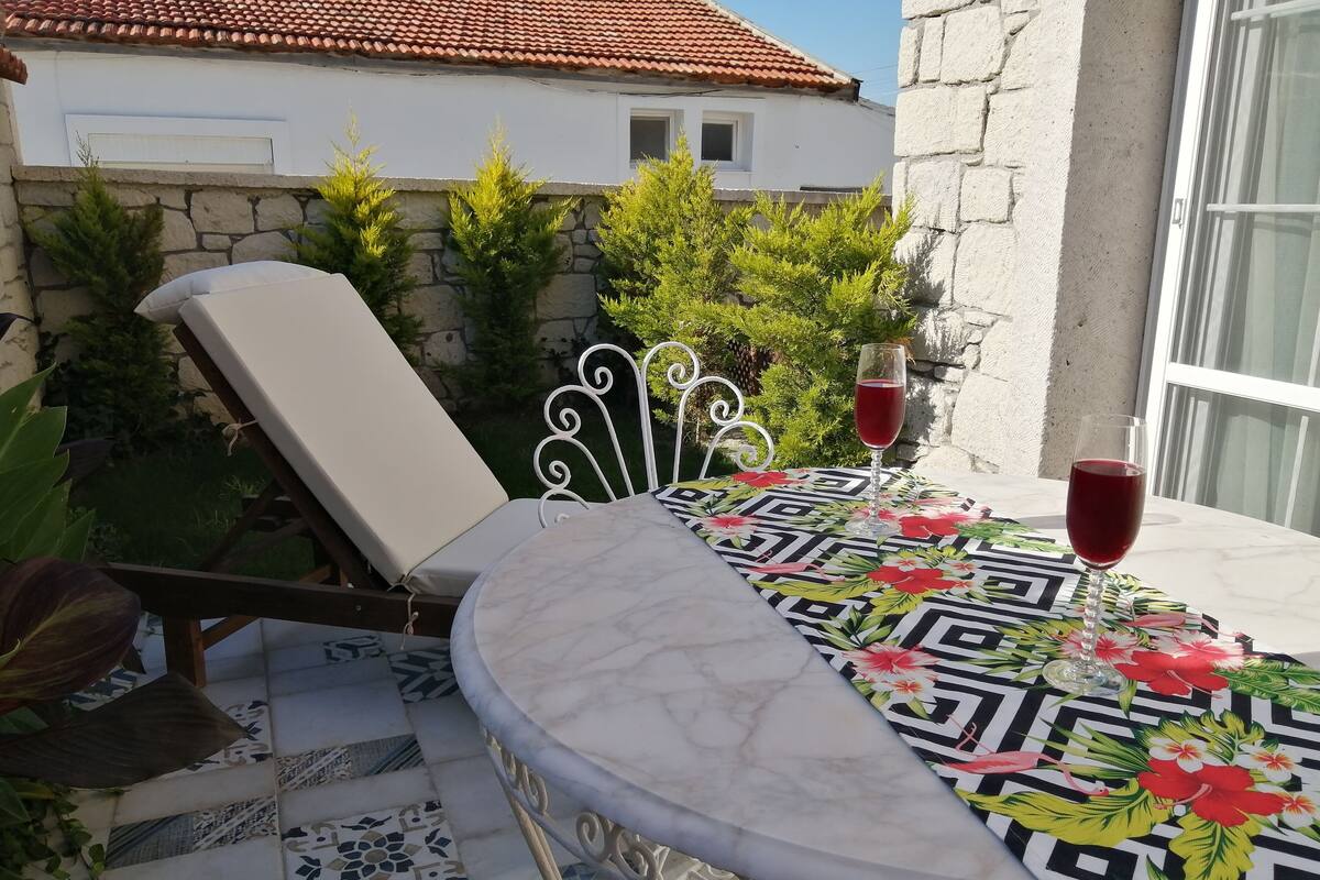 Un espacio al aire libre iluminado por el sol con una mesa, una silla y una copa de vino tinto.