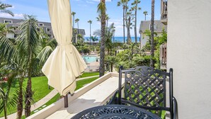 A balcony with a table and chair, overlooking a pool and palm trees. - F204 North Coast Village Tropical Garden & Ocean Views-1 bdrm condo Close To Beach (Oceanside)
