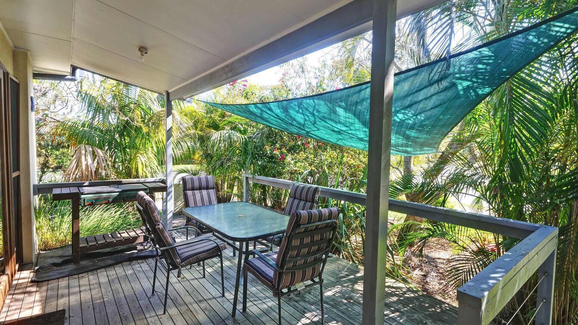 A covered outdoor seating area with a table and chairs, surrounded by lush greenery.