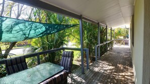 A covered outdoor area with a table and chairs, surrounded by lush greenery and a view of the outdoors.