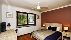 A bedroom with a bed, two bedside tables with lamps, a ceiling fan, and a window with blinds.
