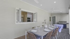 Un coin repas avec une table dressée pour six personnes, un barbecue et une cuisine en arrière-plan.