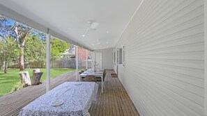 A covered outdoor dining area with a table set for four, a wooden deck, and a view of a backyard with a fence and trees.