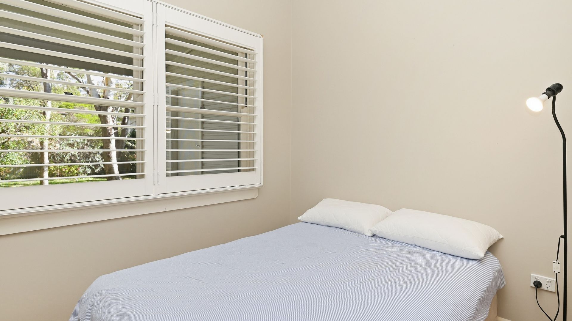A bedroom with a bed, a window with blinds, and a wall socket.