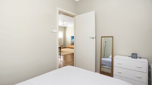 Une chambre à coucher comprenant un lit, une commode, un miroir et une porte donnant sur une autre pièce.