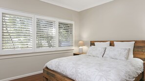 Ein Schlafzimmer mit einem Bett, einem Nachttisch, einer Lampe und einem Fenster mit Jalousien.