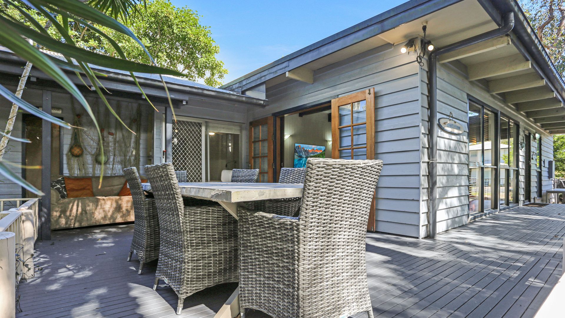 Un espacio de comedor al aire libre techado con mobiliario de mimbre y vista a la casa.
