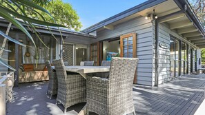 A covered outdoor dining area with wicker furniture and a view of the house. - Bennett's Beach Cottage (Hawks Nest)