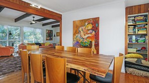 A dining area with a wooden table and chairs, a large painting on the wall, and a bookshelf filled with books.