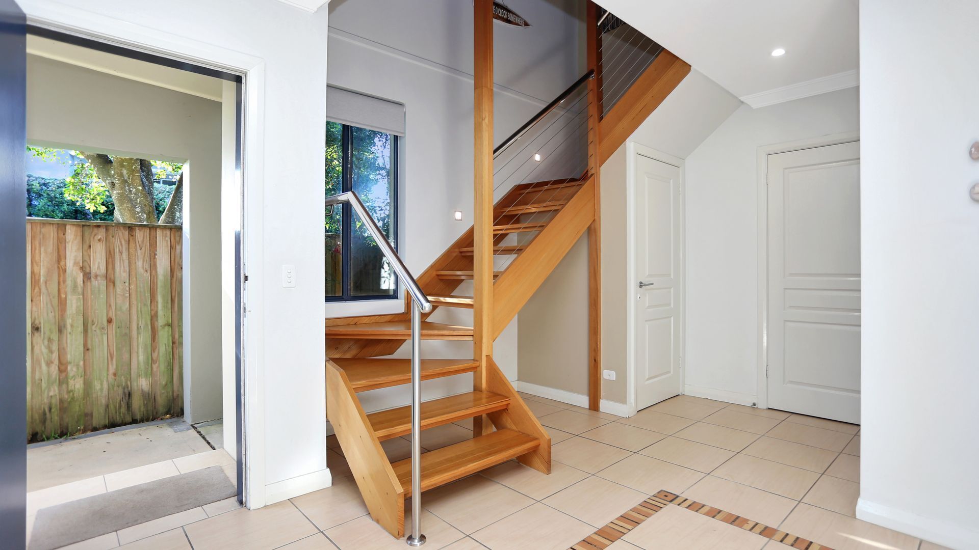 A modern interior with a wooden staircase, a door, and a view of the outdoors.