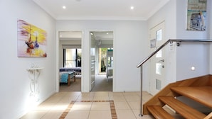 Un intérieur moderne avec un escalier en bois, un lit recouvert d’une courtepointe à motifs bleus et blancs, et un tableau représentant des voiliers accroché au mur.