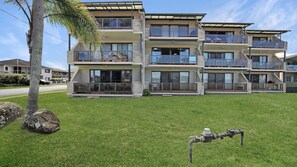 A multi-story residential building with balconies, large windows, and a grassy lawn.