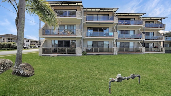 A multi-story residential building with balconies, large windows, and a grassy lawn.
