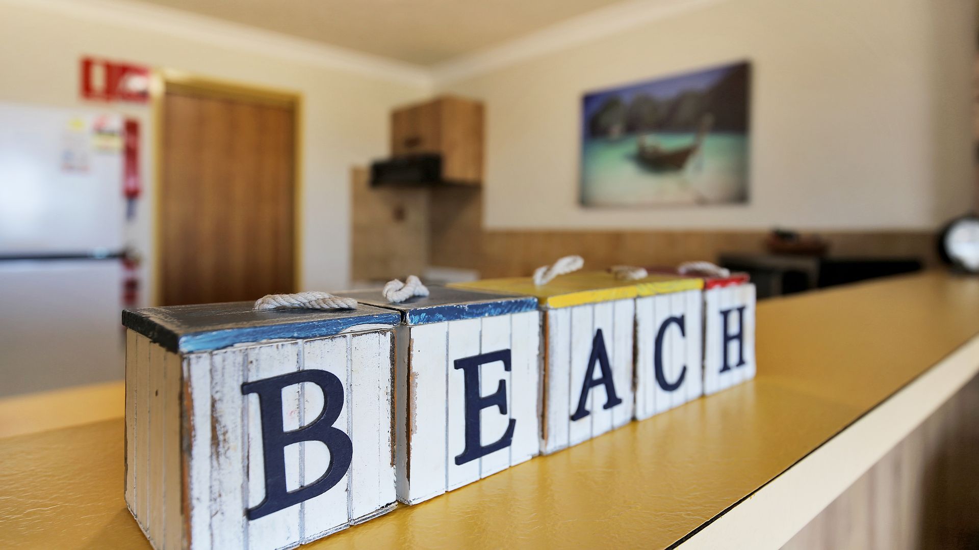 A kitchen counter with wooden blocks spelling 'BEACH' and a painting of a boat on the wall.