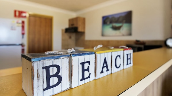 A kitchen counter with wooden blocks spelling 'BEACH' and a painting of a boat on the wall.