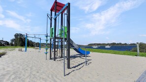 A playground with a slide and climbing structures, located near a body of water.