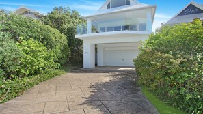 Une maison moderne à deux étages avec un garage, entourée d’une végétation luxuriante.