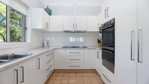 Een moderne keuken met witte kastjes, een roestvrijstalen spoelbak, een gasfornuis en een inbouwoven.