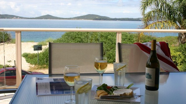 Ein Tisch mit einer Weinflasche, Gläsern und einem Teller Essen mit Blick auf Strand und Meer.