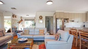 A modern living room with a sofa, coffee table, and dining area. There is a kitchen with cabinets and appliances.
